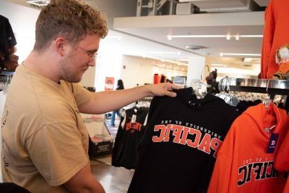 an alumni holds a black sweatshirt that reads University of the Pacific